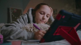Young Caucasian girl lies on bed at home, writes in notebook and does online school lessons using digital tablet. Teenage girl spends time and studies in cozy bedroom in daytime. Lifestyle concept. - Powered by Shutterstock - Get 15% off with code: PIKWIZARD15