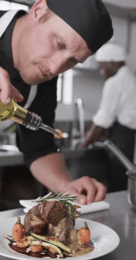 Focused caucasian male chef pouring olive oil on prepared meal in kitchen, slow motion, vertical. Cooking, profession, food, restaurant and catering, unaltered. : vidéo de stock