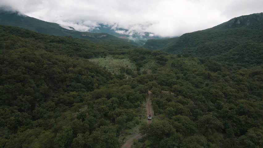 Aerial view of a white Cherokee truck driving trhough the forest in a spectacular moutain landscape, drone shot