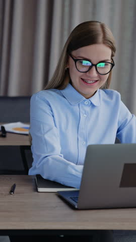 Female office employee working on her laptop. Blonde woman wearing glasses typing messages to the company partners. Vertical video. Royalty-Free Stock Footage #3459720785