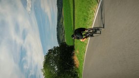 Cyclist riding fast downhill on road bicycle. Vertical video. Professional athlete in sport clothes speeding downhill on bike. Cycling training