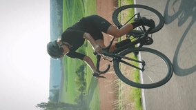 Sportive fit woman in cycling apparel and helmet riding road bicycle uphill through picturesque countryside landscape. Vertical video. Stylish cyclist cycling on bike in mountains