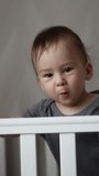 Little boy standing up and sitting down in the cot. Adorable Caucasian child being active after waking up. Vertical video.