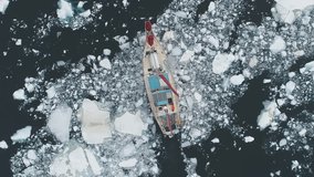Close-up view of Sailing Yacht Break Through Antarctic Melting Ice. Ocean Aerial Top Down Shot. Red Vessel Expedition to Polar Nature Glacier Explore Global Warming Concept Top Drone Shot Footage