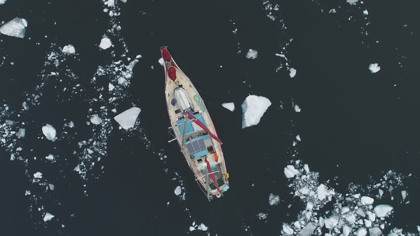 Close-up view of Sailing Yacht Break Through Antarctic Melting Ice. Ocean Aerial Top Down Shot. Red Vessel Expedition to Polar Nature Glacier Explore Global Warming Concept Top Drone Shot Footage