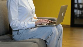 Slow motion. Businesswoman sitting on the grey couch and working on her computer