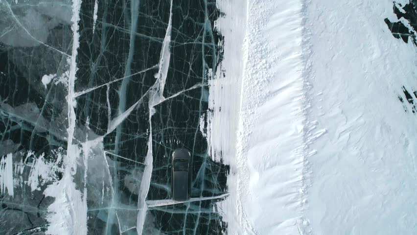 Aerial top down view on a car driving on an ice road on frozen Baikal. Winter landscape of lake Baikal. Drone follows the car