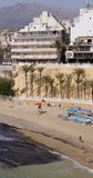 Portrait footage of the beautiful town of Benidorm showing the Cala del Mal Pas Beach on a sunny summers day in the summer time by the boating harbour with people sunbathing on the sandy beach