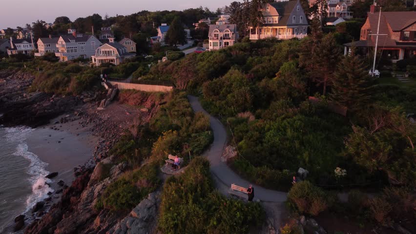 Aerial sunset of Ogunquit Maine USA drone fly above waterfront house luxury resort revealing Marginal way trail path on Atlantic Ocean coastline 