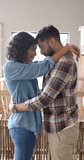 Vertical video of portrait of happy biracial couple embracing and smiling at home, slow motion. Lifestyle, togetherness and domestic life, unaltered.