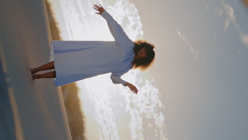 Round mirror reflecting woman dance at sand desert in front sunset vertical oriented. African american girl wearing white dress making graceful hands movements in wilderness. Performance on nature.