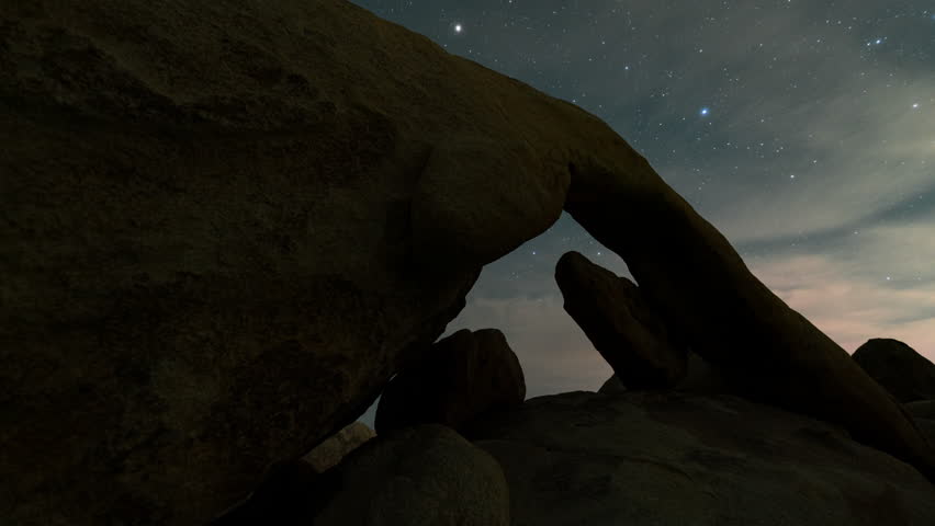 Timelapse tracking shot of Milky Way galaxy rising through arch rock in Joshua Tree National Park, California 