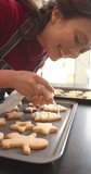 Vertical video of happy biracial woman decorating chistmas cookies in kitchen, slow motion. Food, cooking, christmas, celebration, domestic life and lifestyle, unaltered.
