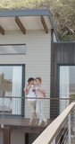 Vertical video of happy diverse gay male couple drinking coffee on balcony at home, slow motion. Lifestyle, togetherness and dometic life, unaltered.