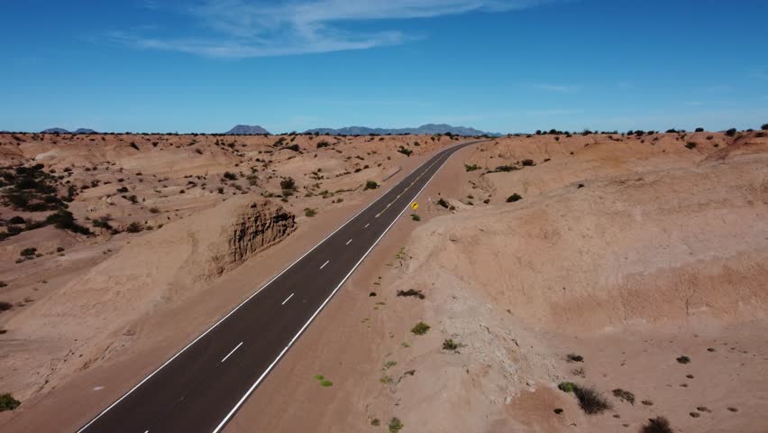 Aerial follows clean, clear highway through red rock badland landscape