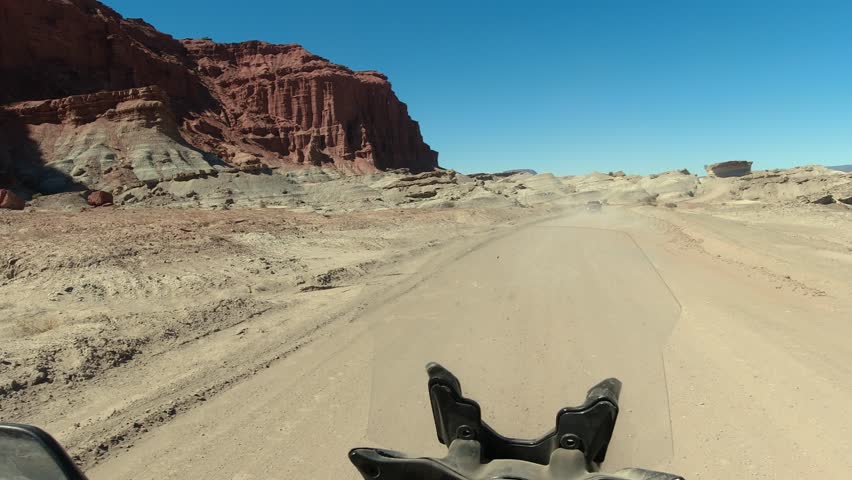Motorcycle POV: Rider follows vehicle on badlands canyon dirt road