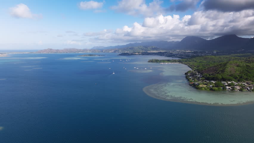 Aerial view of Waikane small village town on sunny day. Cinematic nature landscape on Oahu Island coastline, Hawaii. Shallow waters at tropical island. Beautiful seascape with deep blue Pacific ocean