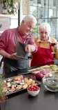 Vertical video of senior caucasian couple cooking dinner in kitchen, slow motion. Senior lifestyle, food, meal, recipe, communication, healthy living, togetherness and domestic life, unaltered.