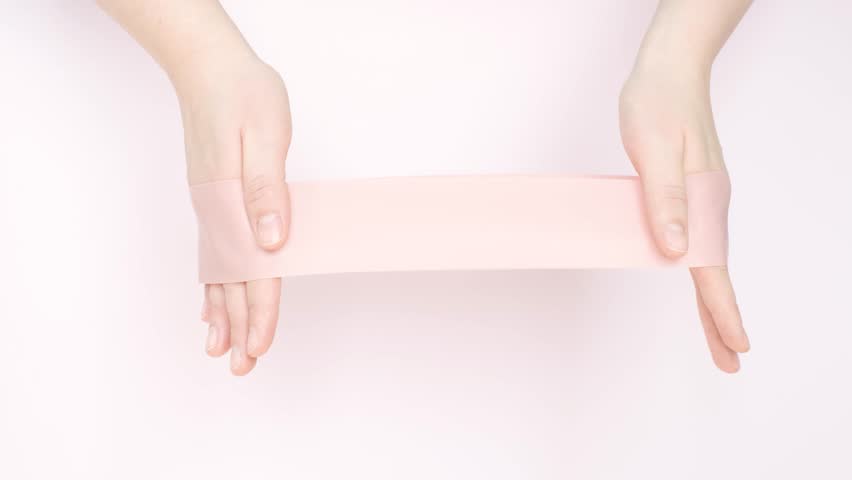 Female hands stretching fitness elastic band on pink background close-up.