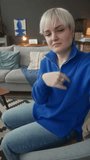 Vertical handheld POV of young Caucasian non-verbal woman speaking sign language at camera while recording video blog at home
