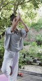 Vertical video of biracial woman practicing yoga on sunny terrace, slow motion. Lifestyle, wellbeing in nature, yoga, fitness, healthy lifestyle and domestic lifestyle, unaltered.