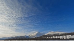 Explore the breathtaking beauty of Yakutia in this mesmerizing time-lapse video. Witness majestic mountains, a frozen river, and drifting clouds against the vivid blue sky.
