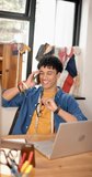 Vertical video of biracial male fashion designer talking on smartphone in studio, slow motion. Fashion, design, creativity, clothing, technology, communication and small business, unaltered.