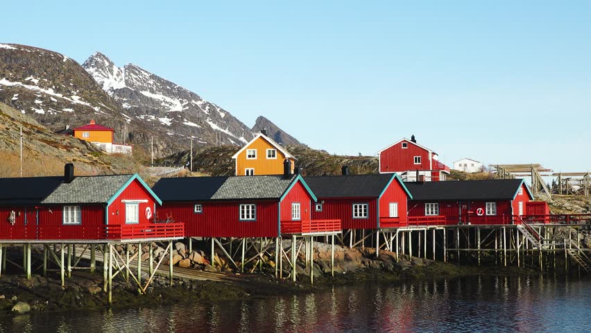 Red wooden Rorbu cabins  in the Lofoten Islands. Traditional fishing village, with red rorbu houses against snowy surroundings. The tranquil landscape is beautifully reflected in the water. Norway.