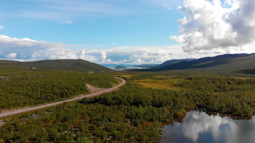 Aerial: Main road in northern Sweden among forests and lakes with very light traffic and with a blue sky and some clouds in the background