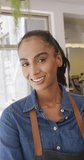 Vertical video of portrait of happy biracial female barista in her cafe shop. Cafe, barista and business concept.