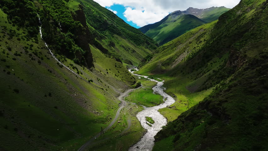 Serpentine River Carving Through a Lush Valley with Green Peaks Under a Cloudy Sky