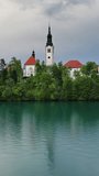Aerial around view of Bled lake with the Pilgrimage Church of the Assumption of Maria on a small island after sunset, Slovenia. Vertical video