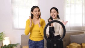 Two young influencer Asian woman dance while live-streaming an online sales event on social media from home.
