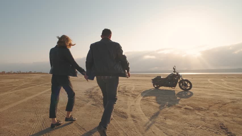 Guy with a girl on a motorcycle in the desert. Couple riding on vintage motorcycle and having a good time at sunset on a dry salt lake. Slow motion shot