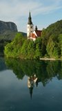 Aerial view of Bled lake with the Pilgrimage Church of the Assumption of Maria on a small island in morning light, Slovenia. Vertical video