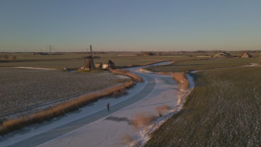 Aerial view of people ice skating on frozen river near old windmill