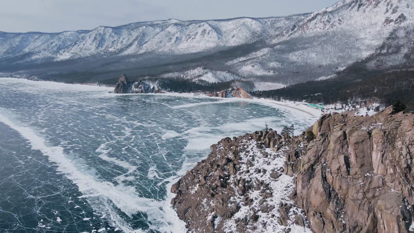 Fantastic aerial view over snowy mountain range. Beautiful landscape of frozen Baikal lake bay and white peaks. Drone shot of amazing natural ice pattern on lake. Concept of nature, landscape travel.