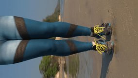Vetical video. Close-up of young sporty female working out with skipping rope on beautiful sandy beach in the morning, slow motion