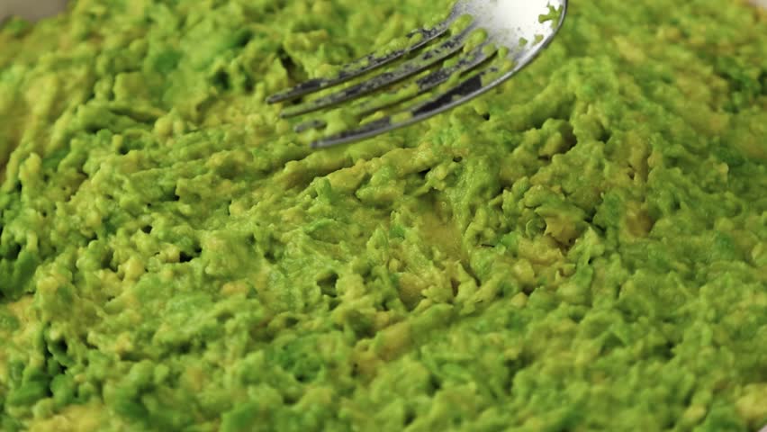 Mashing avocado with a fork dip rotating in ceramic plate close up background. Cooking healthy food. Making avocado guacamole.