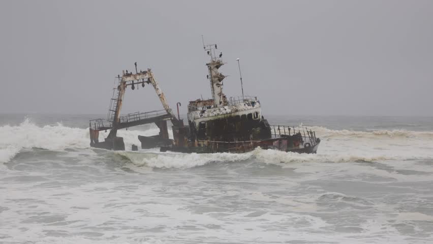 Shipwreck Zeila in the crashing waves at sea from beach near Swakopmund on Namibia Skeleton Coast, Africa under grey solemn sky. Royalty-Free Stock Footage #3460701527