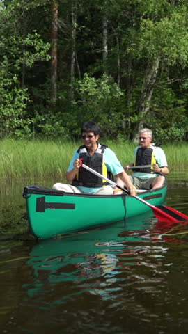Senior couple canoeing on a forest lake in Finland. Active retirees enjoy outdoor sports. Sportive elderly people having fun at the nature. A vertically-oriented video.