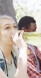 Vertical video of happy diverse couple drinking water in park, slow motion. Nature, hiking and park concept.