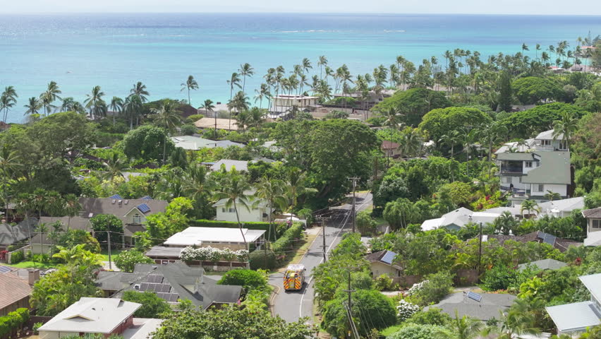 Aerial view over ambulance vehicle driving by Oahu island Hawaii. Yellow first responders car rushing to arrive to emergency situation at Lanikai beach. Aerial panorama small town with scenic beach 4K