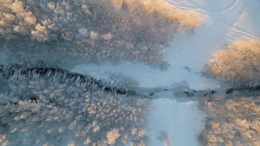 Aerial Nordic Winter Landscape, Snow falling on Frozen river through forest