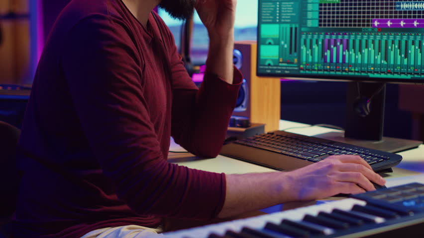 Music producer engages in post production with editing and time aligning recorded songs. Musician using digital audio workstations to manipulate tunes, adding audio effects. Camera A. Royalty-Free Stock Footage #3460768981
