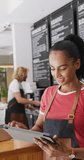 Vertical video of happy diverse male and female baristas using tablet in cafe. Cafe, barista and business concept.