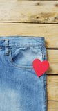 Vertical video of denim trousers with red heart with copy space on wooden background. Denim, clothes and fashion concept.