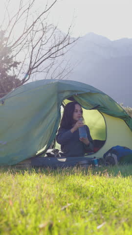 vertical shot. the child drinks water. a child sits in a tent and drinks water from a bottle. boy in a sleeping bag. portrait of a child in a tent. camping and trekking with children.