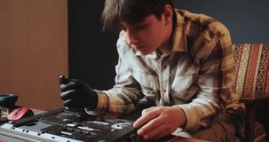 A teenager sits thoughtfully over a disassembled laptop. Careful attitude to technology. Repair and refurbishment of equipment
