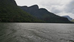 Rolling water flows through a lush green canyon flanked by tall mountains standing tall amidst sub-tropical vegetation under a cloudy, white, and grey sky. - Powered by Shutterstock - Get 15% off with code: PIKWIZARD15